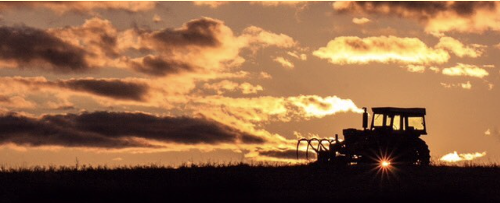 sun peeks through farm equipment at sunset
